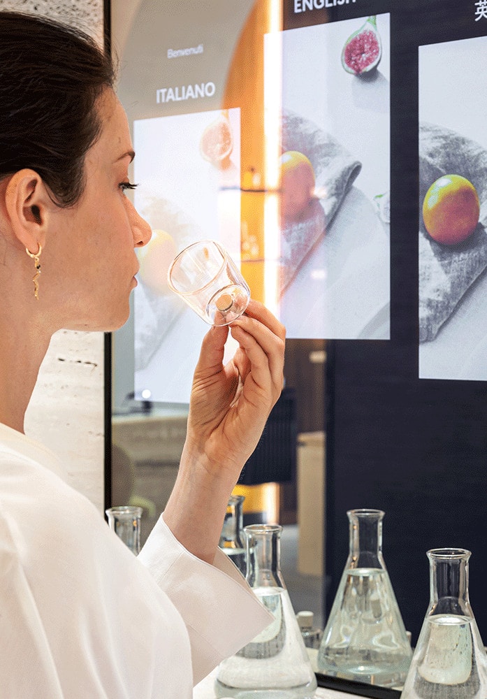 donna che annusa una boccetta di profumo davanti allo specchio interattivo realizzato da ett per la postazione fragrance finder acqua di parma