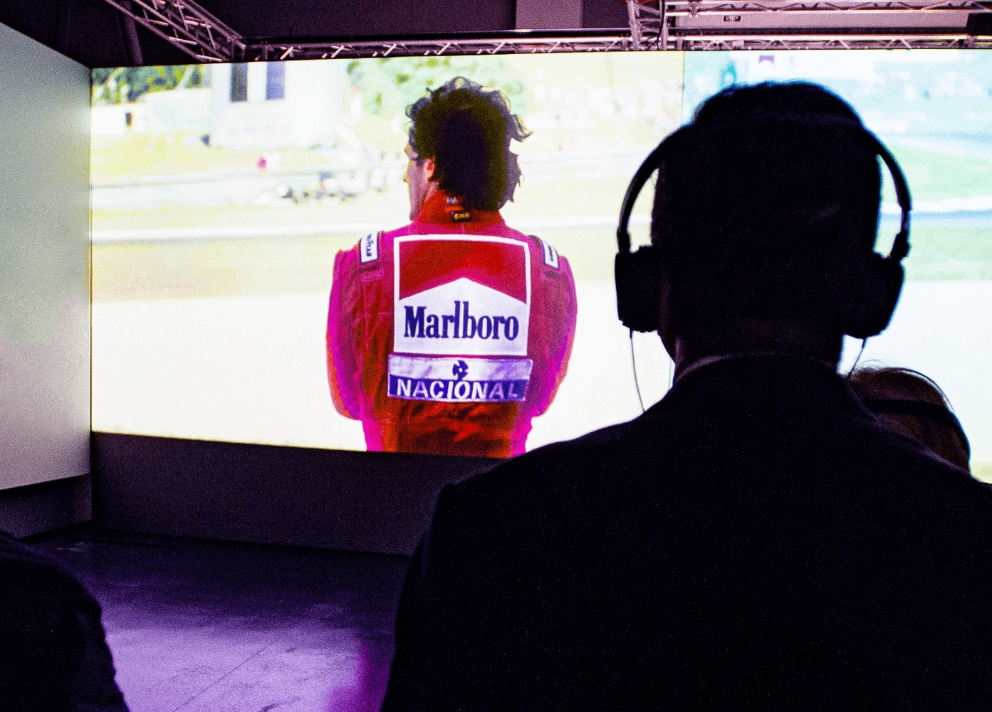 uomo con cuffie che osserva una proiezione della mostra Ayrton Senna