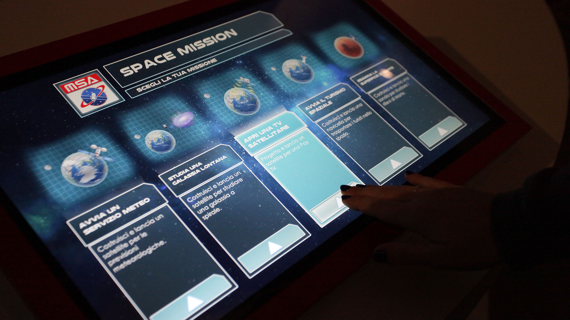 mano che tocca e interagisce con MUST interactive pad con schermata della msa space mission dove poter scegliere il proprio viaggio nello spazio, realizzato da ett