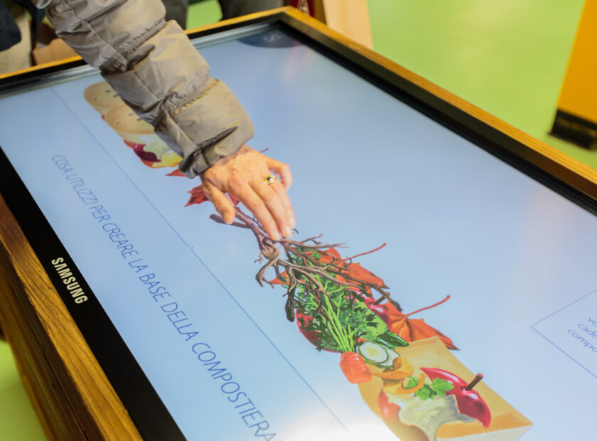 mano di una donna che tocca uno schermo samsung interattivo nel museo a come ambiente di torino, progetto realizzato da ett