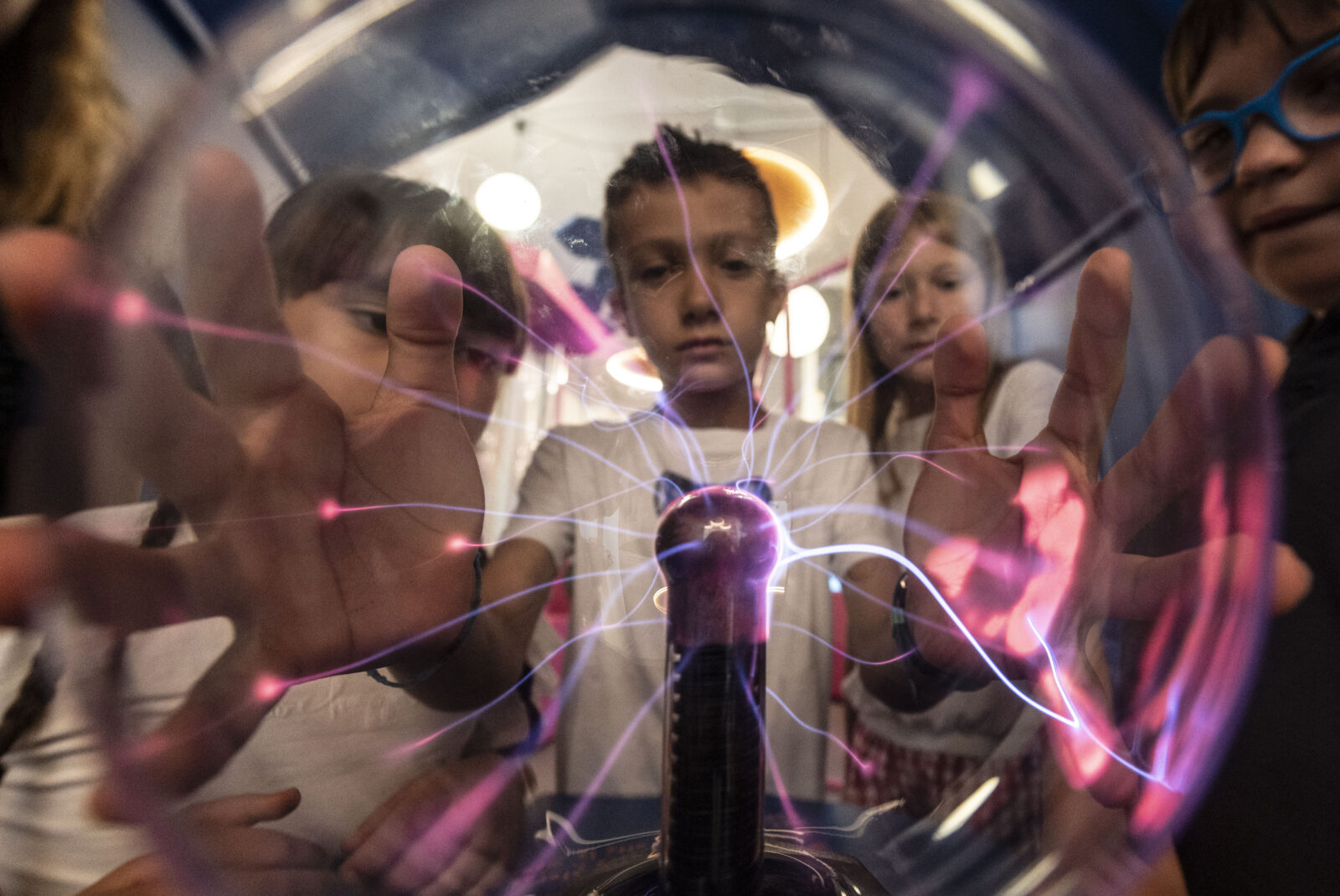 Bambino che tiene in mano una sfera trasparente con energia elettrica viola che si dirama dalle sue mani, parte dell'allestimento del MU-CH, museo della chimica, realizzato da ett