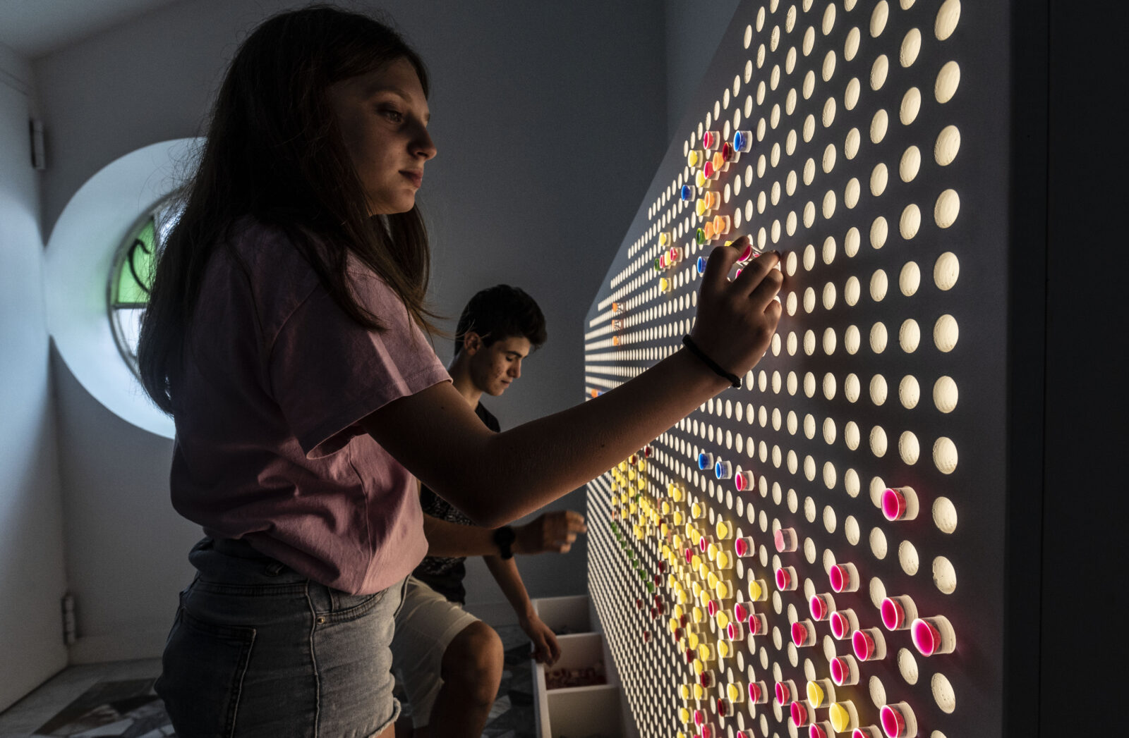 bambina che gioca con delle provette colorate inserendole in una parete forata in una stanza del mu-ch, museo della chimica, il cui allestimento è stato realizzato da ett