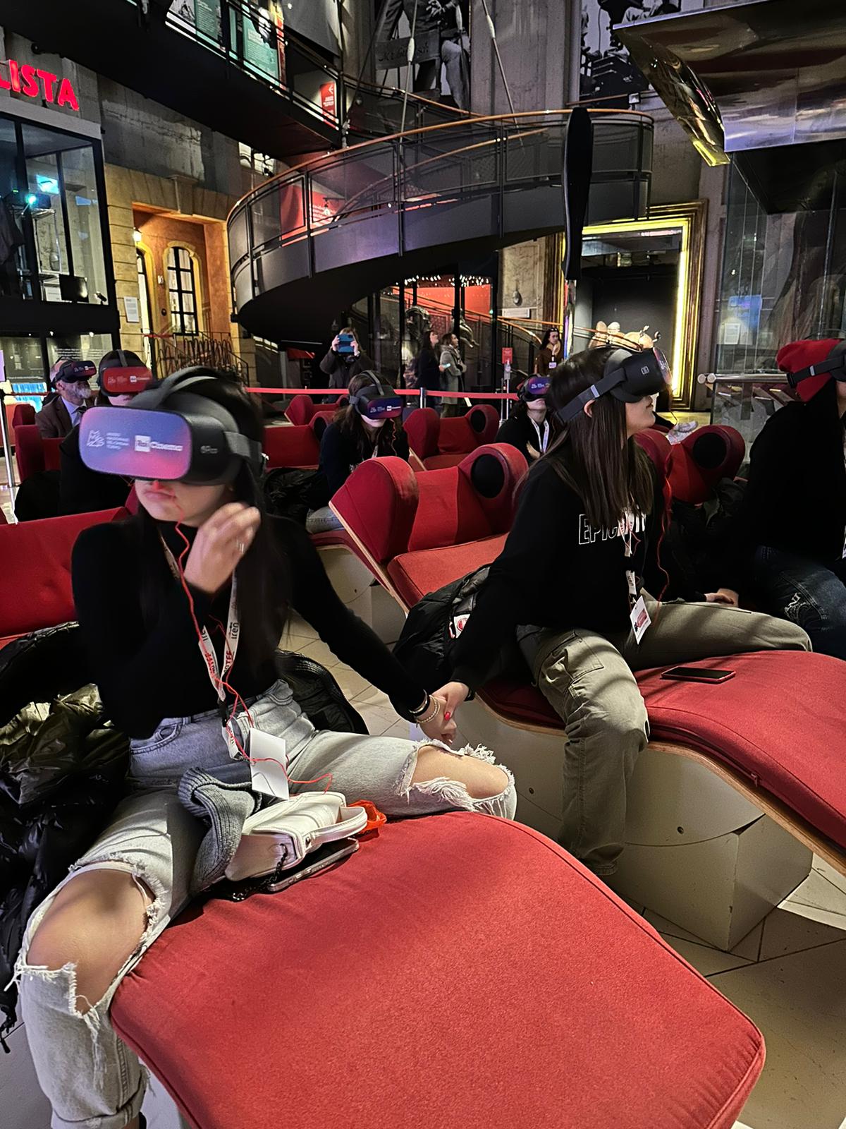Ragazze sedute sulle poltrone del museo del cinema di Torino che utilizzando il visore per vedere la Divina commedia VR realizzata da ETT e distribuita da Rai Cine