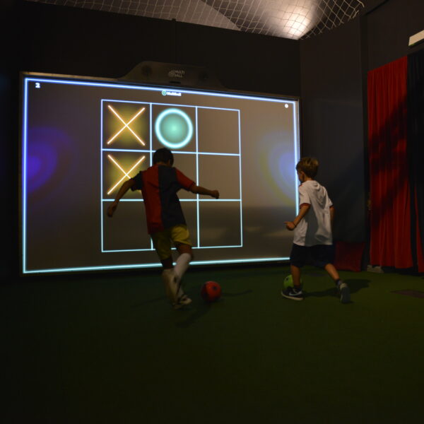 due bambini vestiti da calciatori che nella penombra tirano dei calci a un pallone all'interno del museo del genoa, intenti a giocare ad un gioco interattivo in cui devono fare tris su uno schermo gigante