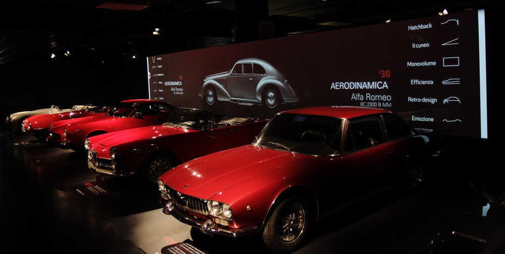 mostra dell'auto all'interno del mauto a torino, 5 modelli rossi di alfa romeo con dietro un'istallazione video di ETT