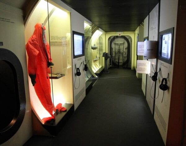 foto all'interno di un corridoio del sommergibile Nazario Sauro, ricostruzione del museo del mare galata. sulla sinistra delle teche con oggetti del capitano, schermi interattivi e cuffie attraverso cui descrivere la vita di Nazario Sauro