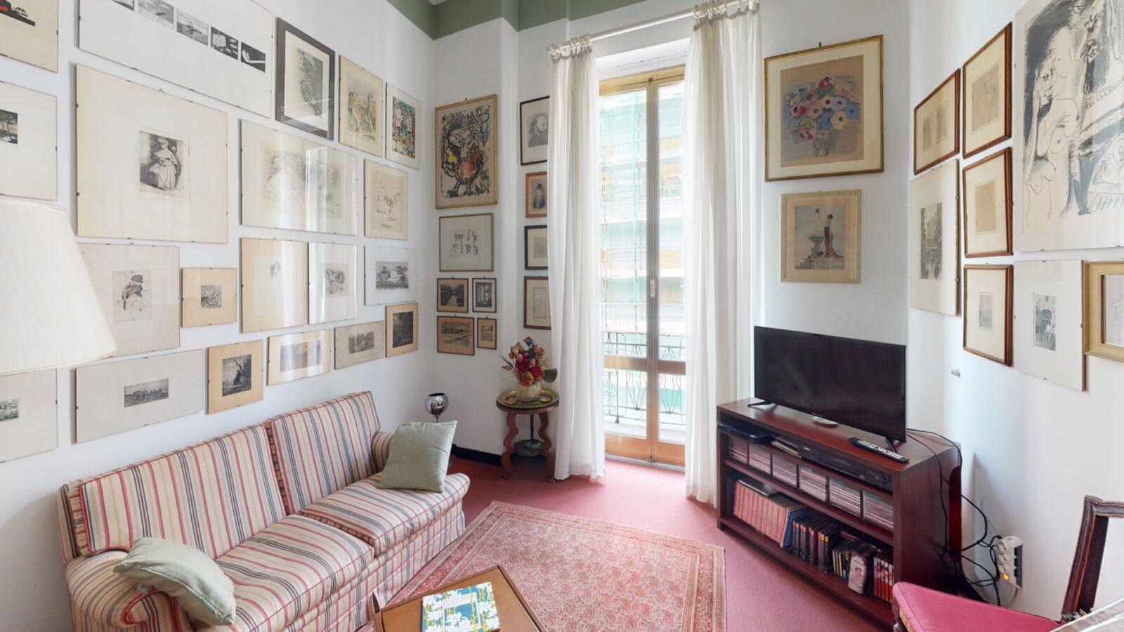 una delle stanze di Fondazione Mario Novaro, un salotto con divano e mobile con tv, le pareti ricoperte di quadri