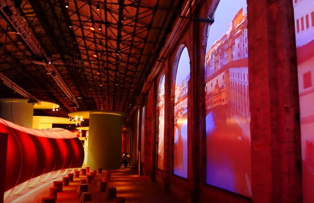 parete sui toni del rosso all'interno dell'allestimento nella stazione leopolda per i 50 anni di Unicoop Firenze, sulla parete di destra proiezioni dei paesaggi toscani
