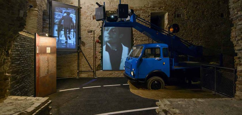 Una sala del nuovo Fellini Museum a rimini, riproduzione di un momento di riprese esterne, sul fondo schermi che riproducono scene di film felliniani, allestimento a cura di ett