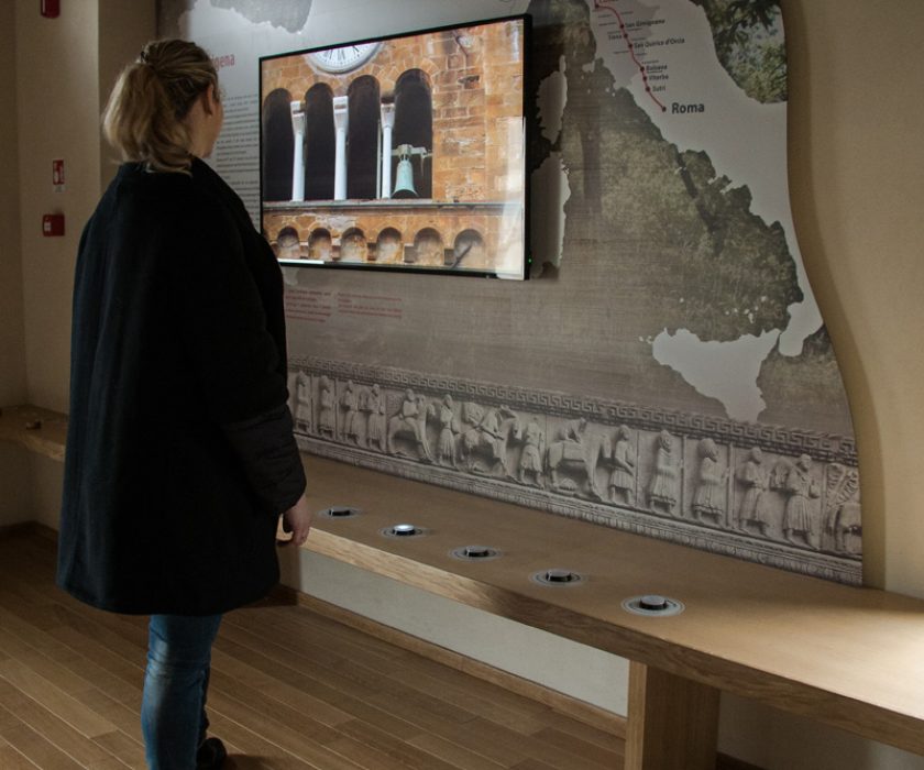 donna davanti all'installazione sul muro di Via Francigena, mappa interattiva con schermo, realizzata da ett, che permette ai visitatori di scoprire le vicende storiche europee nella strada che parte da roma e arriva a calais