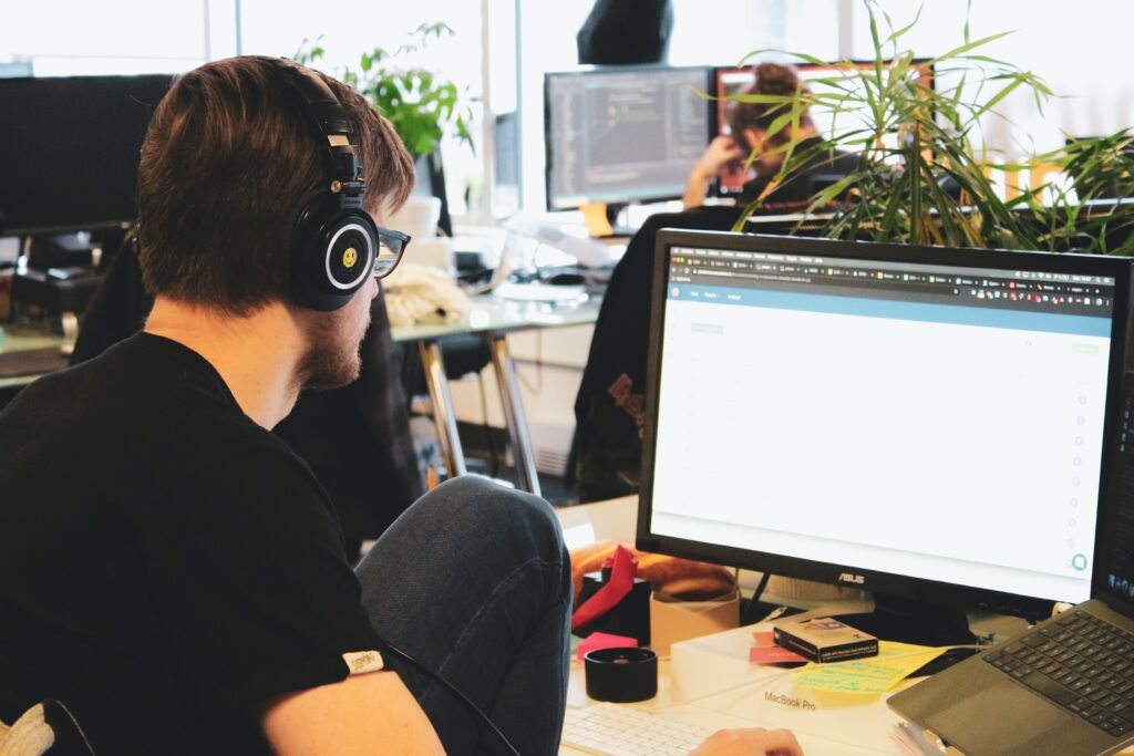 ragazzo davanti alla scrivania con le cuffie che lavora al computer in un ufficio open space