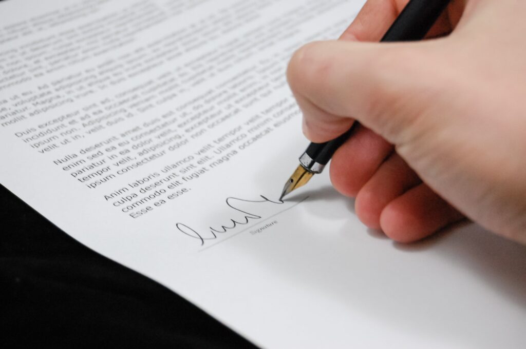 zoom su una mano con una penna stilografica nera che firma un documento scritto