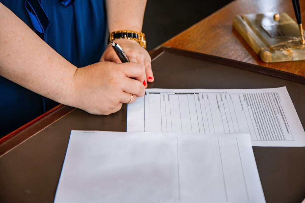 mani di una donna con le unghie rosse che sta firmando un documento sulla scrivania di un avvocato