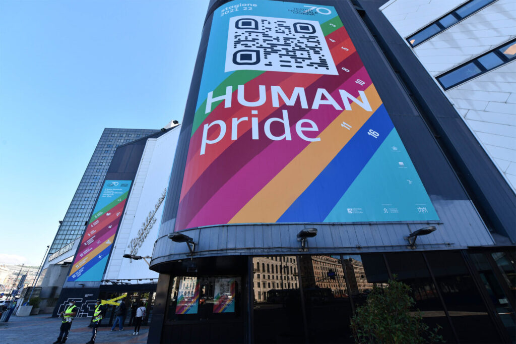 foto all'esterno del QR code gigante 'human pride' su sfondo arcobaleno, sulla parete del Teatro Nazionale di genova, applicazione web di ett che si attiva con la scansione del qrcode