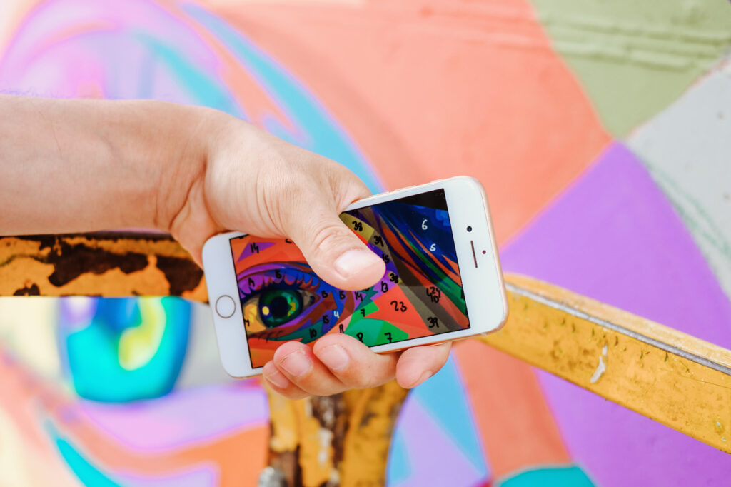 mano che stringe uno smartphone con indicazioni di colore per la realizzazione di un murale nell'ambito di Pintada