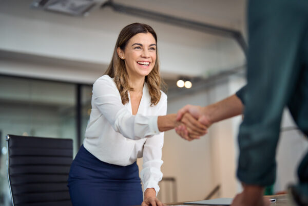 Felice donna d'affari che stringe la mano salutando il cliente in ufficio in piedi al tavolo delle riunioni