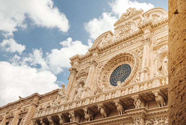foto di una parte alta della facciata della basilica di santa croce a lecce vista dal basso, sull'inquadratura a destra una colonna in primo piano