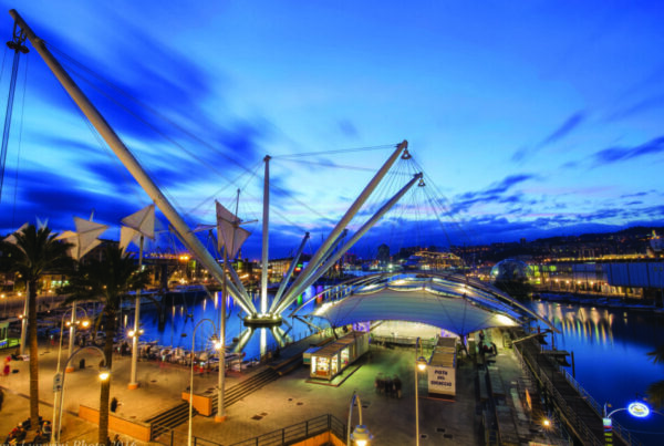 foto del porto antico di genova, in particolare il bigo e la pista di pattinaggio in un paesaggio notturno illuminate dalle luci della città