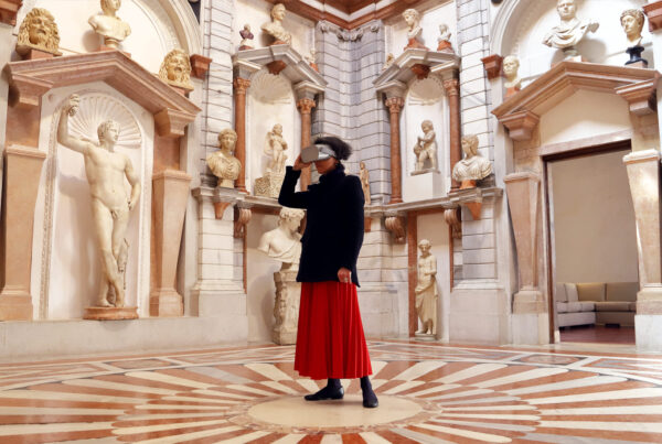 ragazza con una lunga gonna rossa al centro della stanza, domus di palazzo grimani, che indossa visore vr, circondata dalle pareti ricoperte di statue e mezzi busti in marmo