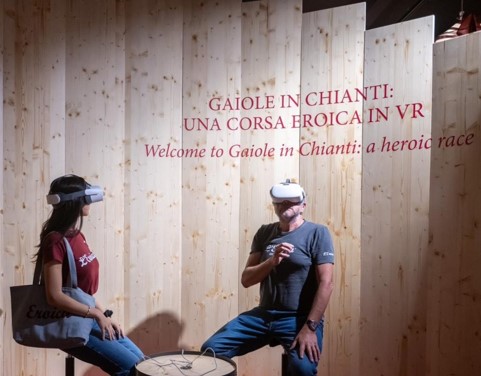 due persone mentre seduti su due sgabelli provano l'esperienza vr, realizzata da ett, all'interno del percorso di casa eroica