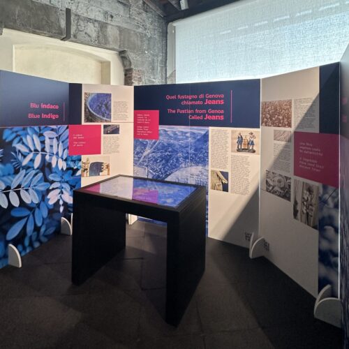 tavolo touch interattivo, realizzato e installato da ETT all'interno del MEI durante Genova Jeans, esposizione dedicata alla storia del denim, dietro un pannello in cui viene raccontato ci che si può vedere nei video sullo schermo del tavolo