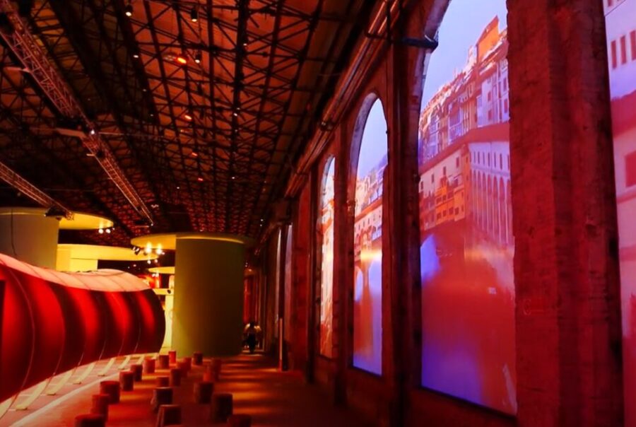 parete sui toni del rosso all'interno dell'allestimento nella stazione leopolda per i 50 anni di Unicoop Firenze, sulla parete di destra proiezioni dei paesaggi toscani